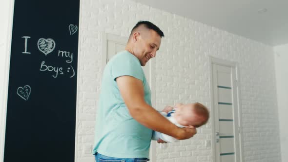 Happy Young Father Playing with His Son Two Months. He Tosses Him, Smiling. Family Comfort and Care