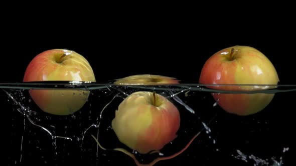 Three Green Apples are Bouncing From Water with Splashes of on Black Background