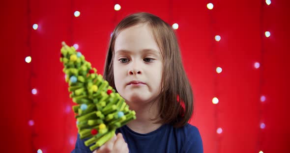 Cute Girl in a Santa Hat Holds a Gift on a Red Christmas Background