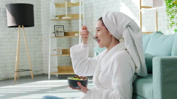 Lady Sitting Near Sofa After Shower and Laughing Eating Granola with Yogurt