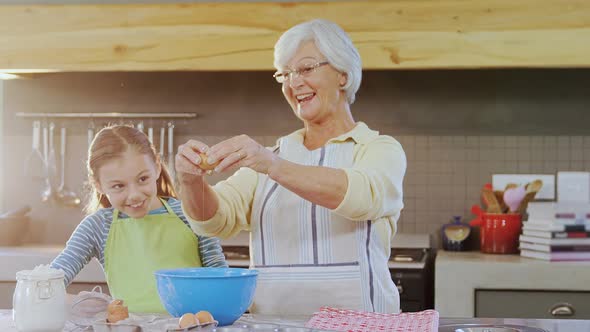 Grandmother breaking an egg in bowl and little girl watching 