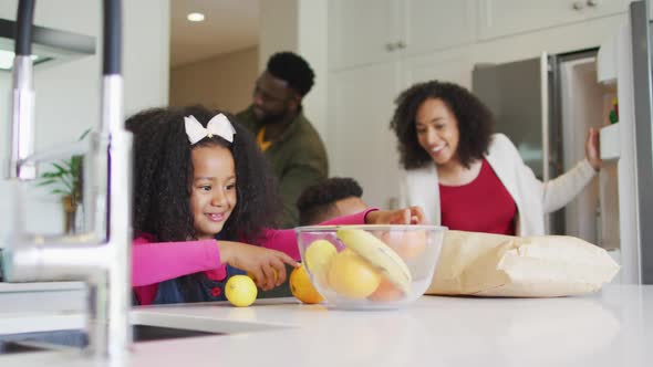 Happy african american girl unpacking groceries in kitchen with parents and brother