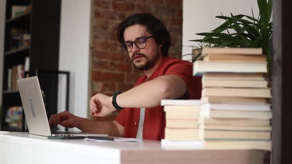 Stylish man sitting at table in home office and using laptop