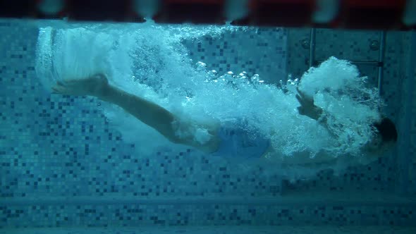 Athlete swimmer dives underwater in a pool with blue water. Super slow motion