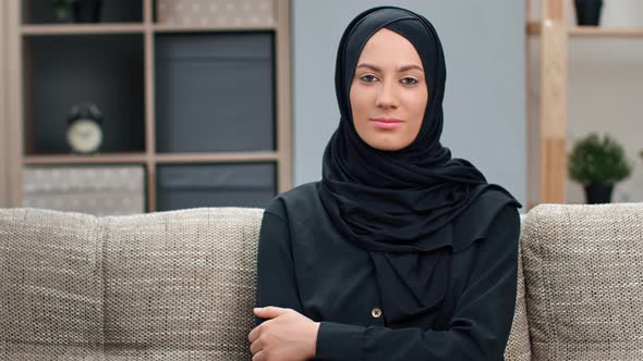 Portrait of Smiling Muslim Woman in Black Hijab Relaxing on Comfortable Couch at Modern Interior