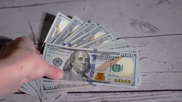 Female Hand Takes a Stack of Fanned Out 100 Dollar Bills Lying on the Table