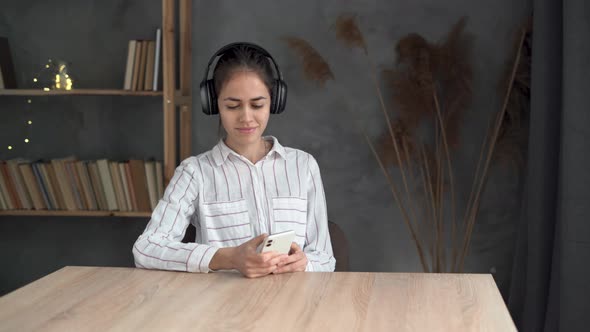 Serene Young Woman Relaxing at Table at Home Wearing Casual Home Clothes Wireless Headphones