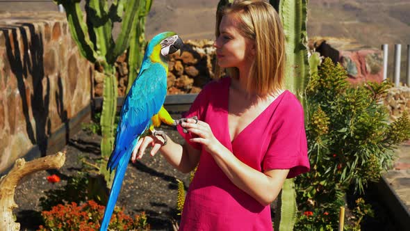 Blonde Model Playing with Macaw Parrot with Cacti and Plants in the Background