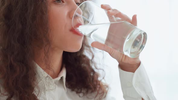 Close up of Latino woman sit on bed drink a glass of water in bedroom.