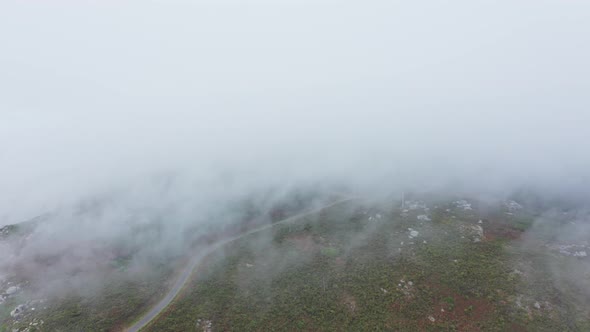 Cinematic drone flight through low clouds with solitary road on hill view