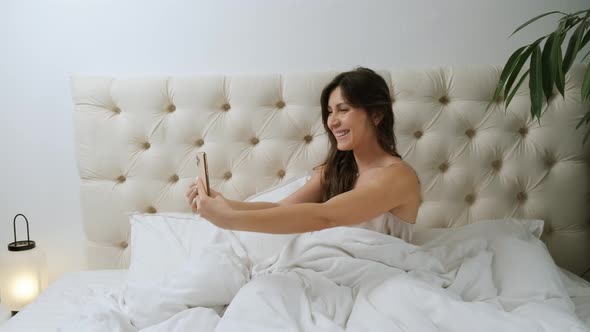 Young Beautiful Woman Sitting in the Bed and Making Selfie in the Morning