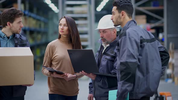 Serious Middle Eastern and Caucasian Men and Woman Discussing Logistics As Warehouse Loader Passing