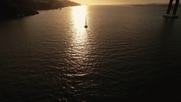 Silhouette of Lone Sail Yacht Going Into the Sunset on River Under a Bridge