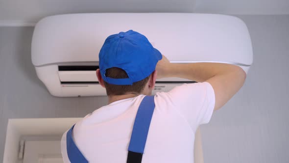 A young master in uniform repairs the air conditioner in the apartment.