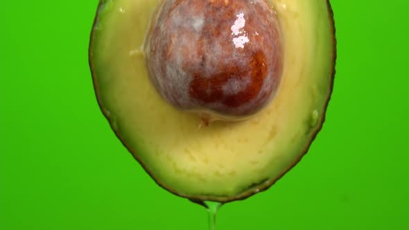 Water drops falling from avocado on green background. Avocado slice and water splashing