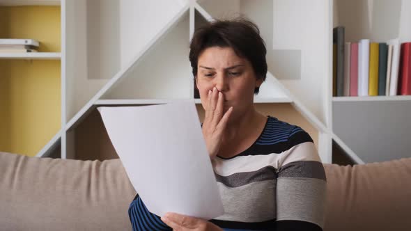 Sad Woman Sitting on Couch at Home Reads Received Bad News Holds Documents Paper
