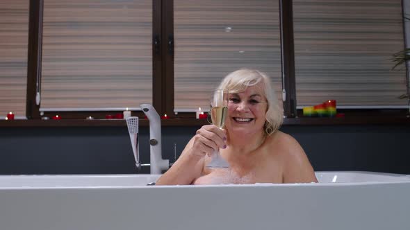 Elderly Senior Woman Lying in Warm Bath with Bubbles, Enjoying Relaxation, Drinking Champagne