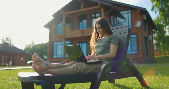 Woman Working on Laptop Sitting in Courtyard of Country House