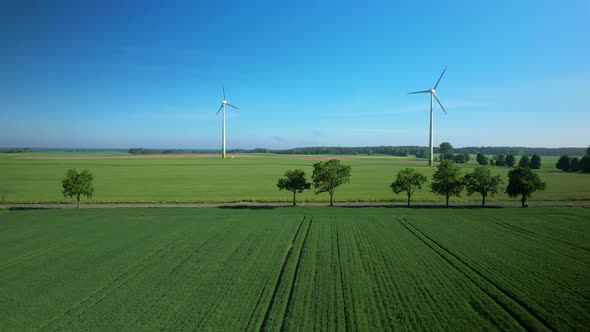 Push in aerial view Sustainable wind turbines spinning on sunny lush rural agricultural farmland