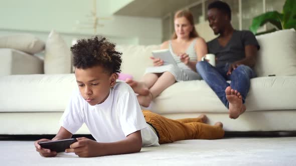 Boy Using Phone and Parents Sitting on Couch with Tablet in Hands at Home Room Spbd