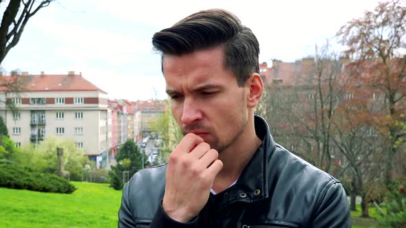 Young Handsome Serious Man Stands and Thinks About Something in Park.