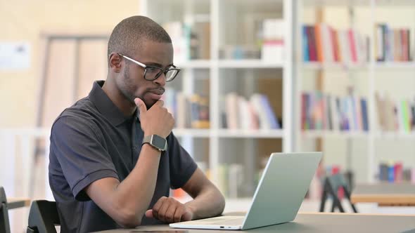 Professional African Man Thinking and Working on Laptop in Library