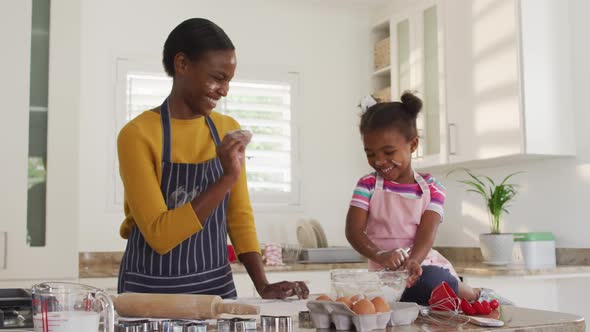 Happy african american mother and daughter wearing aprons having fun while cooking in kitchen