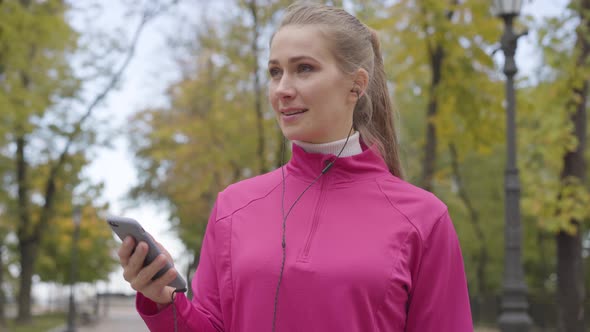 Young Caucasian Woman in Pink Sportswear Turning on Music in Her Headphones and Starting Running