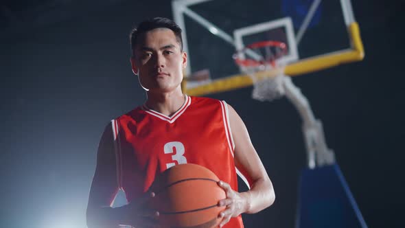 Portrait of an Asian Man Basketball Player Holding a Ball in Her Hands and Serious Looking at the