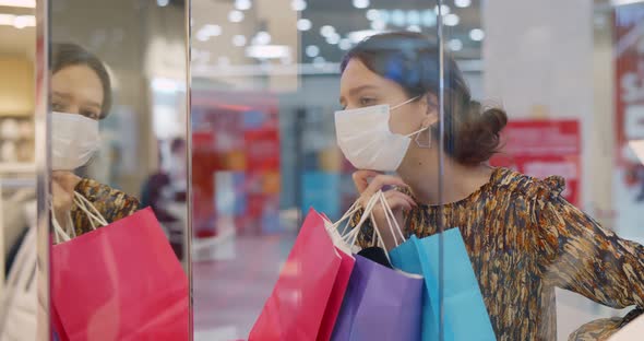 Young Fashionable Woman with Protective Mask and Shopping Bags Looking Through Shop Window