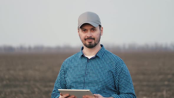 Male Farmer is Working in Field with Digital Computer Looking at Camera Smiling