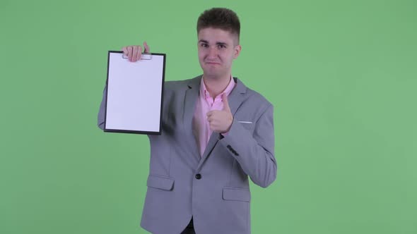 Happy Young Businessman Showing Clipboard and Giving Thumbs Up