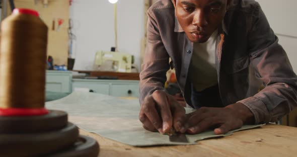 Focused african american craftsman cutting piece of leather in leather workshop
