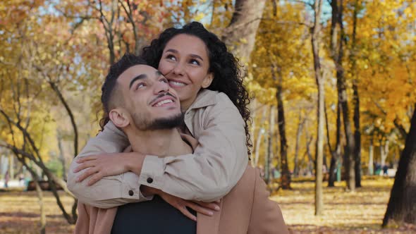 Close Up Happy Hispanic Couple Cuddle on Date in Autumn Park Smiling Partners Look Up Enjoying Sunny