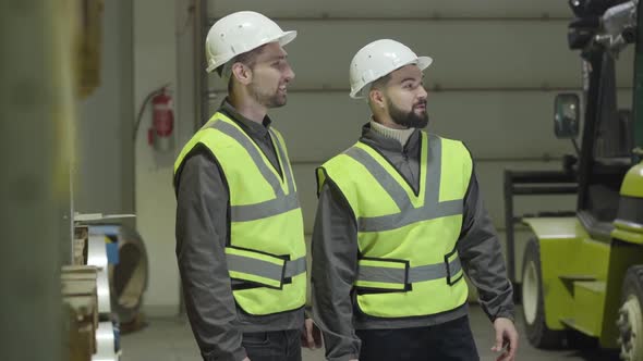 Profile Portrait of Two Caucasian Men Standing at Warehouse and Talking. Employees Working at