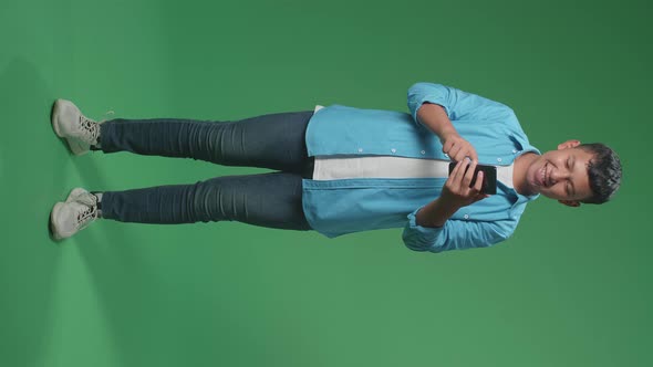 Full Body Of Smiling Young Asian Boy Using Mobile Phone In Green Screen Studio alt