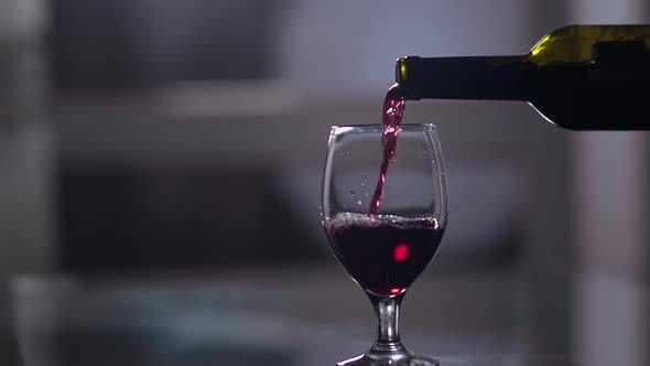 Red Wine Is Poured From a Bottle Into a Glass, Evening at Home, Close Up, Woman's Hand Takes a Glass