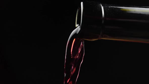 Red wine pouring from neck of bottle in wine glass over dark background. Slow motion