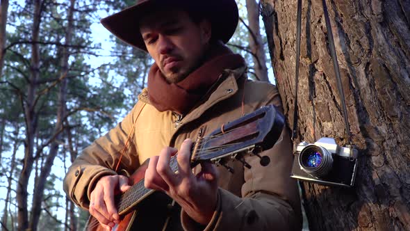 A Backpacker in a Hat with a Guitar in the Forest