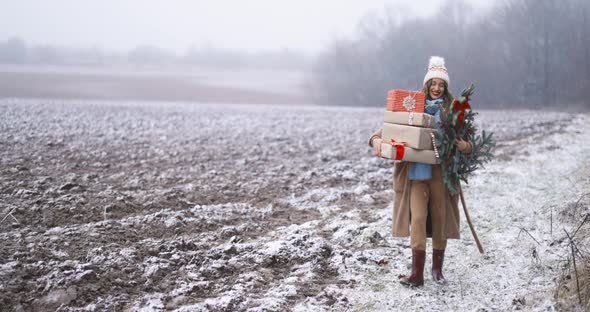 Woman with Gift Boxes and Christmas Branch on the Snowy Field