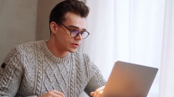 Concentrated man wearing eyeglasses talking by video call on laptop