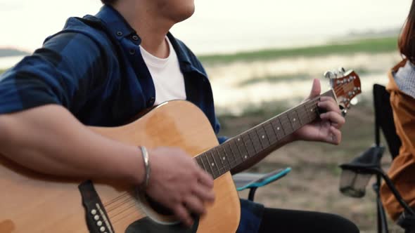 Asian couple camping playing the guitar and singing a song together beside camp.