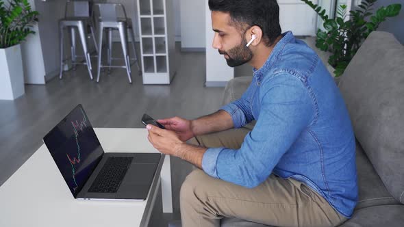 Young Adult Indian Stock Broker Sitting at Home Office Using Digital Devices