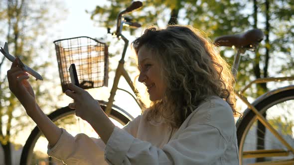 Girl Takes Toy Plane Sitting in Park on Background of Cruiser Bike at Sunset, Slow Motion