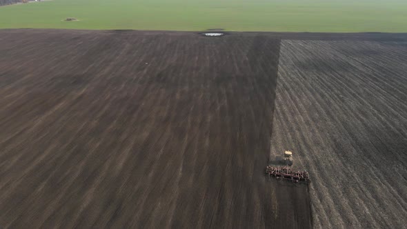 Aerial view of a modern yellow tractor plowing dry agricultural field , preparing land for sowing