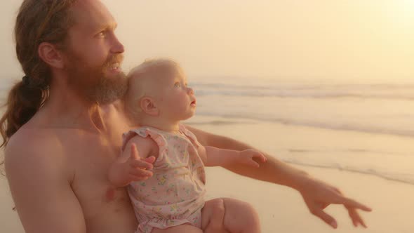 Caucasian Bearded Father Holding Little Baby Infant Small Daughter Son Newborn Standing at Sandy
