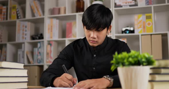 Focused young asian worker man writing paperwork at home