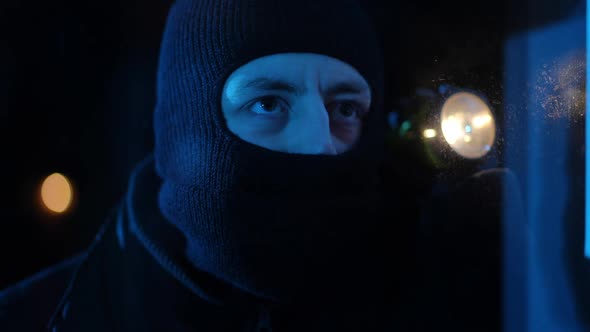 Closeup Concentrated Burglar with Flashlight Looking Through Window Running Away