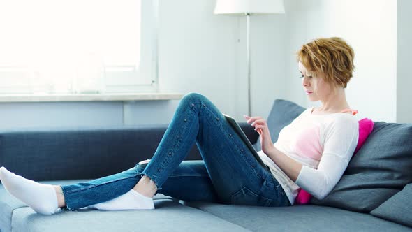 Woman is Lying on the Couch with a Tablet