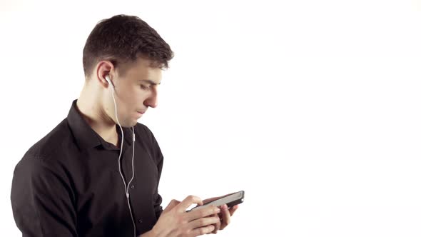 Portrait of Young Handsome Man in Black Shirt and Headphones Listening to Music on His Phone